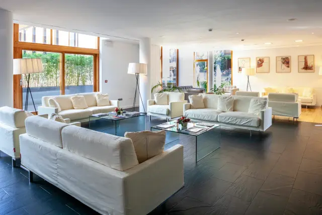 Amplia sala de estar de suite con varios sofás blancos, mesas de centro de cristal y gran ventanal con vistas