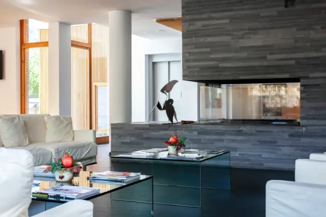 Salón de suite con sofás blancos, mesa de centro con revistas y chimenea moderna de piedra en la pared.