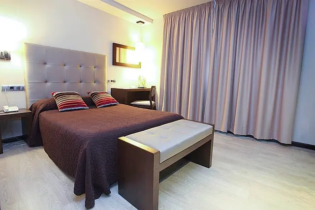 Vista de una suite con cama king size con cabecero tapizado, dos almohadas decorativas, banco tapizado al pie