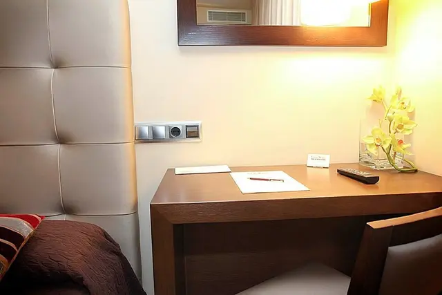 Vista de una habitación de hotel con cabecero acolchado en tonos beige, escritorio de madera con papeles, bolígrafo