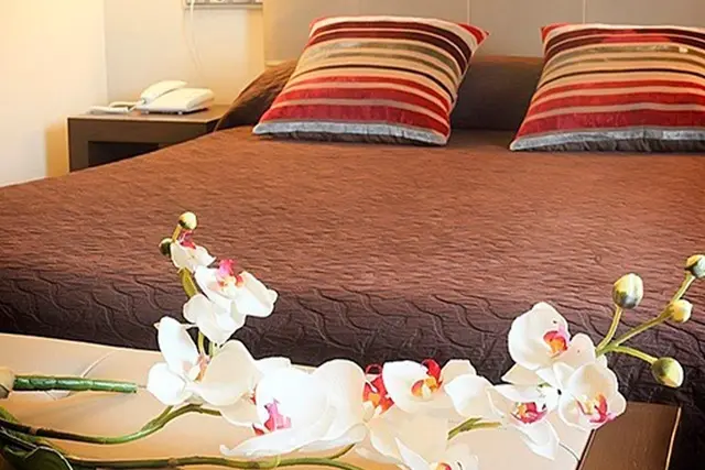 Vista de una cama grande en una suite con edredón marrón y almohadas a rayas rojas, blancas y grises.