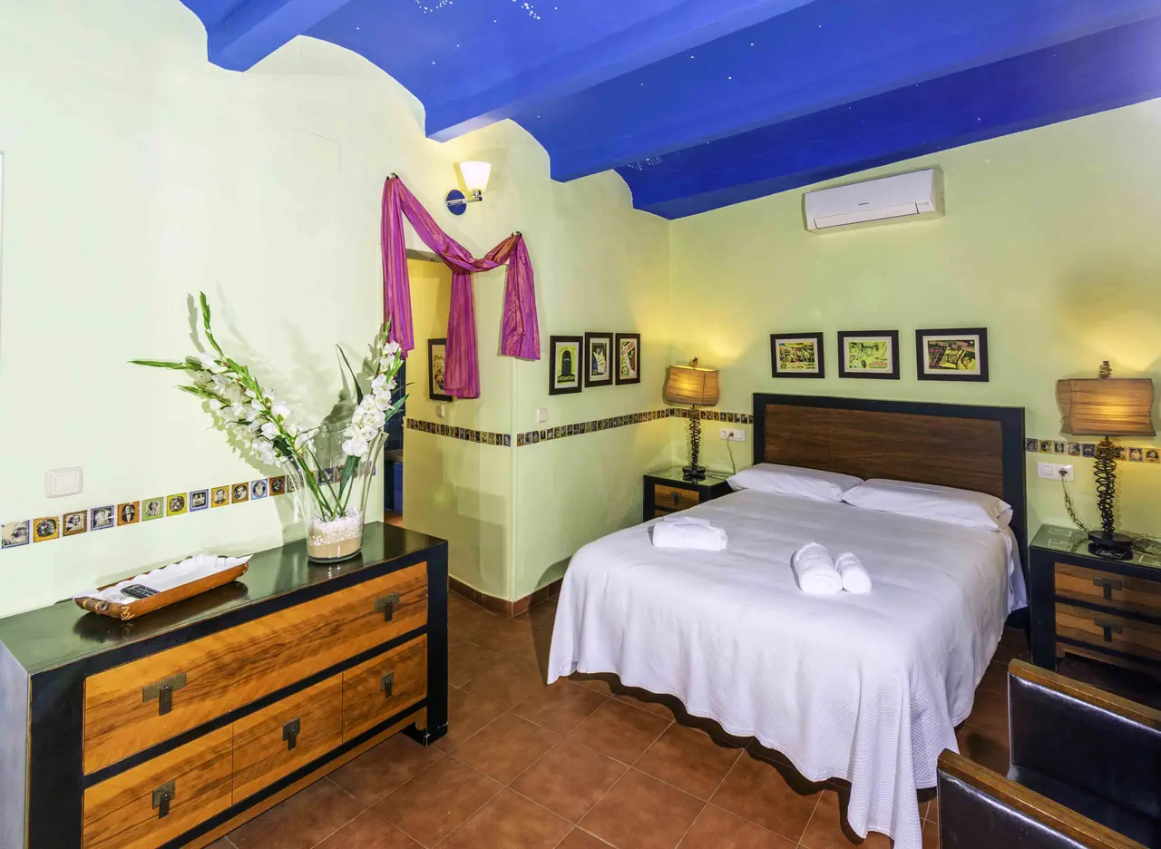 Habitación de hotel con paredes en tonos verde claro y techo azul, cama doble con sábanas blancas y toallas