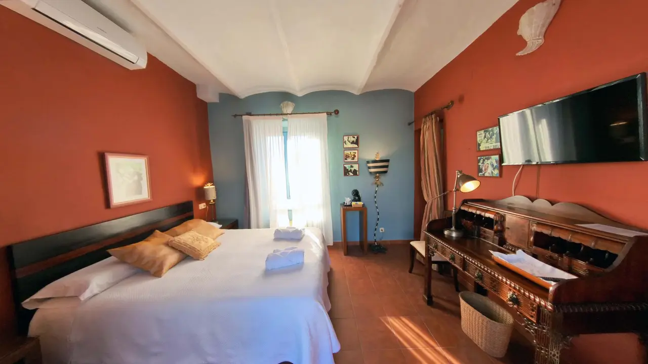 Habitación de hotel con paredes naranjas y una pared azul al fondo. Cama doble con sábanas blancas y almohadas beige
