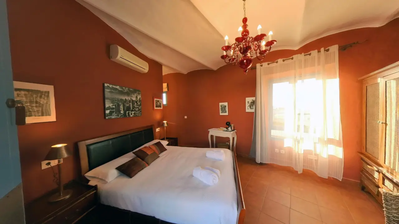 Habitación de hotel con paredes naranjas, cama doble con sábanas blancas y toallas enrolladas, cabecero de cuero