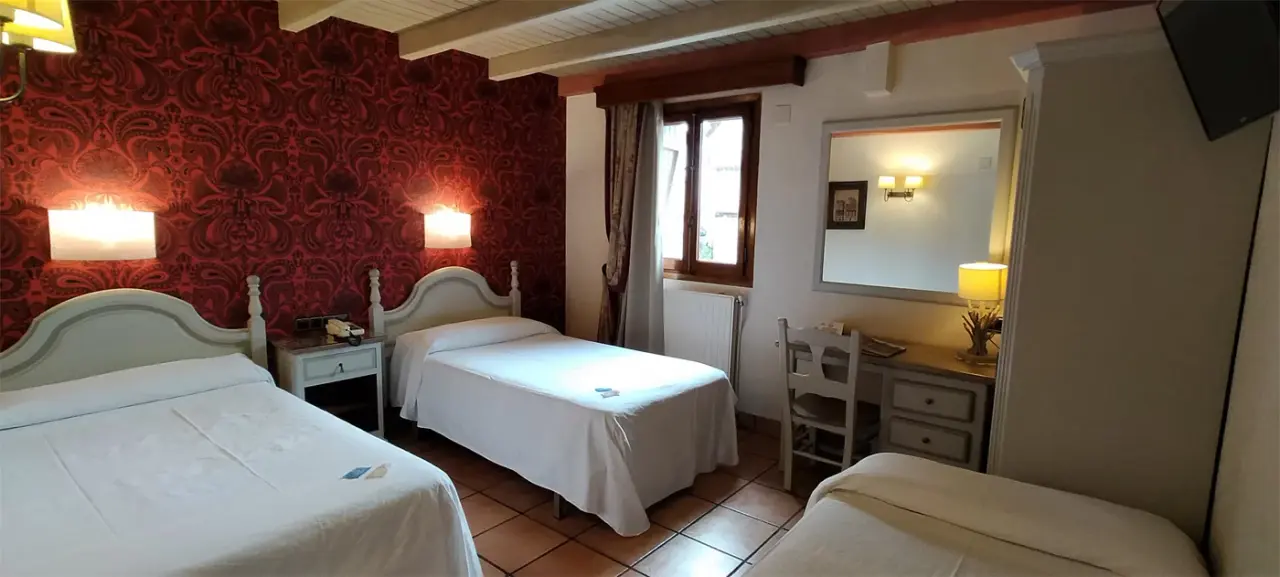 Habitación de hotel con dos camas individuales y una tercera cama plegable, paredes con papel rojo estampado, suelo