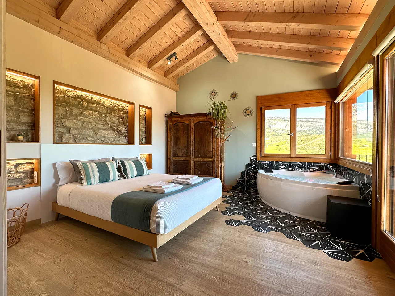 Habitación con cama doble, armario de madera, techo de vigas vistas y jacuzzi redondo en una zona con suelo de mosaico