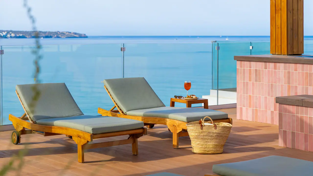 Terraza exterior de una junior suite con dos tumbonas de madera y cojines grises, una mesa auxiliar con una bebida