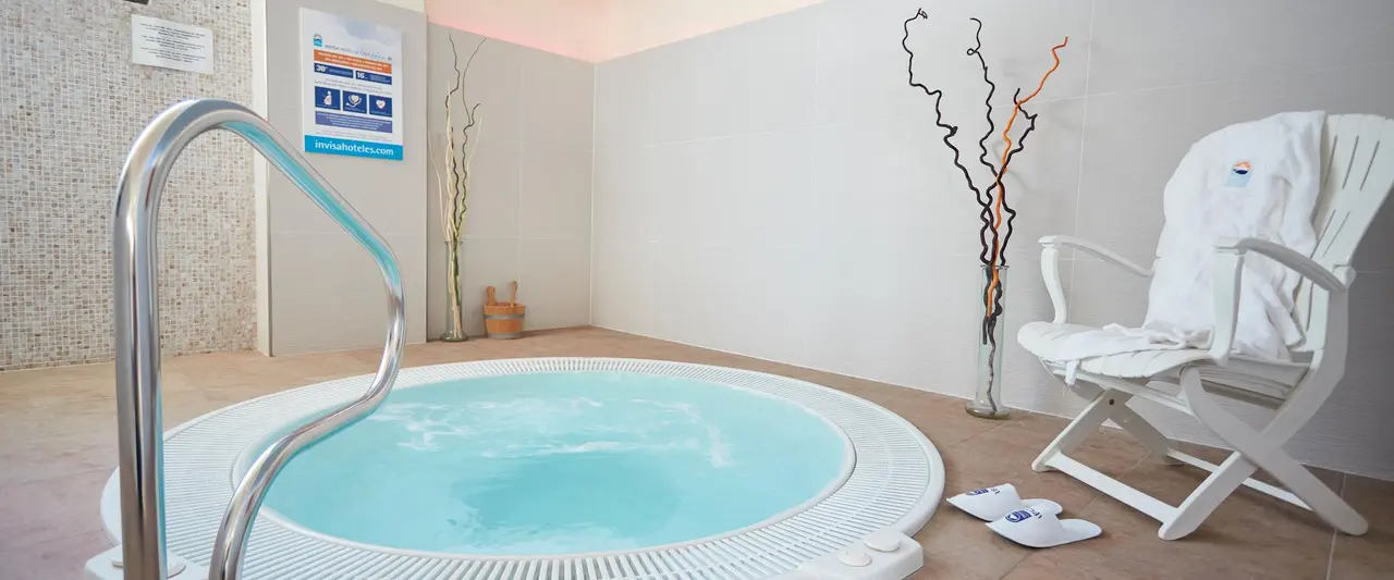 Vista de un jacuzzi circular con agua azul clara y barandilla metálica en una sala de spa privada.