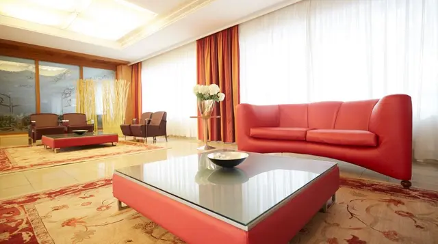 Sala de estar con sofá rojo, mesa de centro de cristal, alfombras y cortinas naranjas, parte del circuito spa privado.