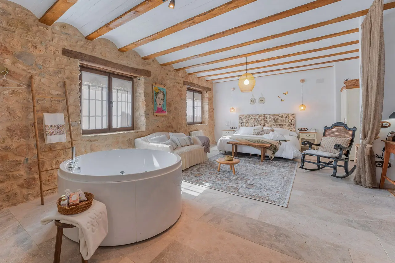 Vista de una suite rural con un jacuzzi privado blanco de gran tamaño en primer plano, suelo de piedra, paredes