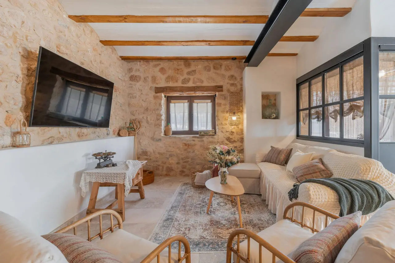 Interior de una sala de estar rústica con paredes de piedra vista, vigas de madera en el techo, un sofá grande