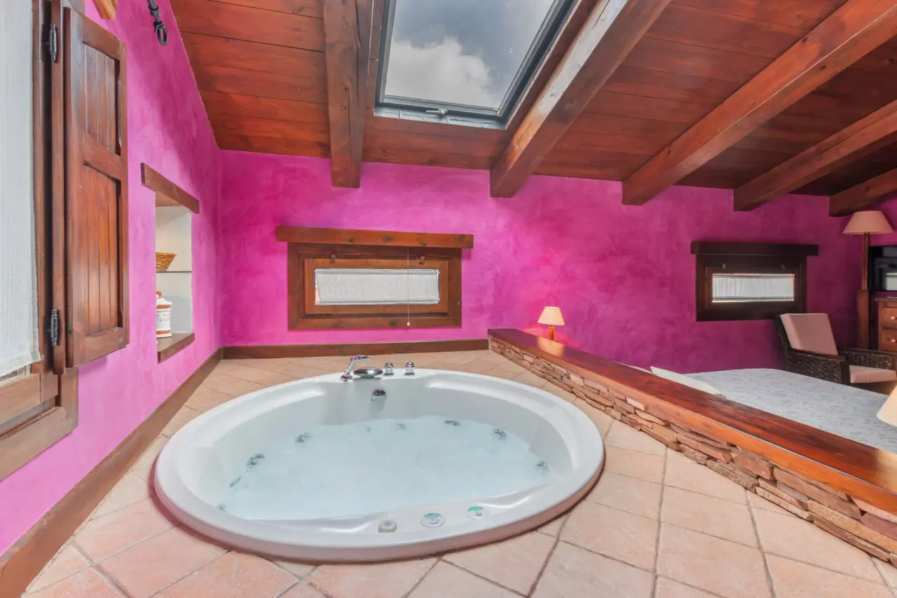 Jacuzzi circular blanco con agua burbujeante en una habitación con paredes magenta, suelo de terracota y techo