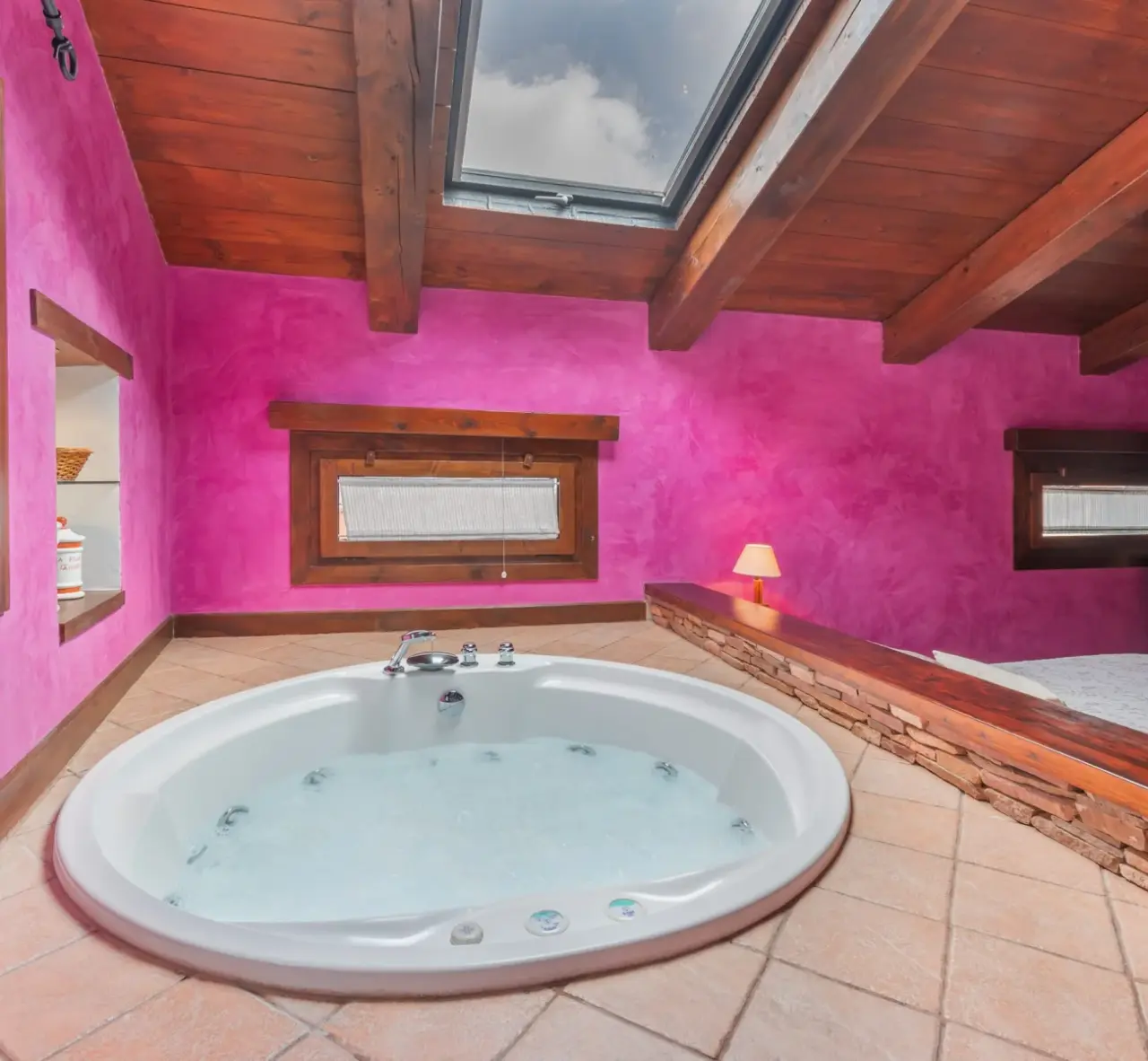 Jacuzzi redondo blanco con agua burbujeante en una habitación con paredes fucsia, suelo de terracota y techo de madera