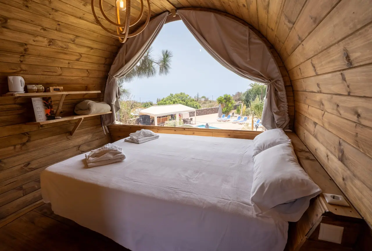 Interior de una habitación con paredes y techo de madera curvada, una cama grande con sábanas blancas y toallas