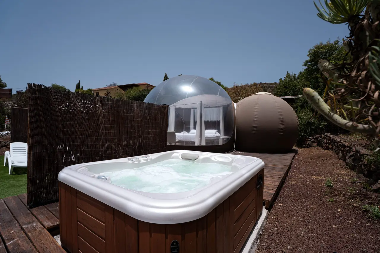 Jacuzzi exterior rectangular con agua burbujeante, situado en una terraza de madera junto a un jardín privado.