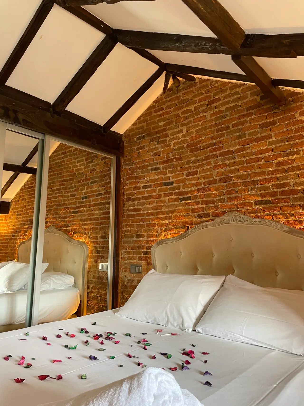 Habitación con cama grande de cabecero capitoné beige, sábanas blancas decoradas con pétalos de flores de colores
