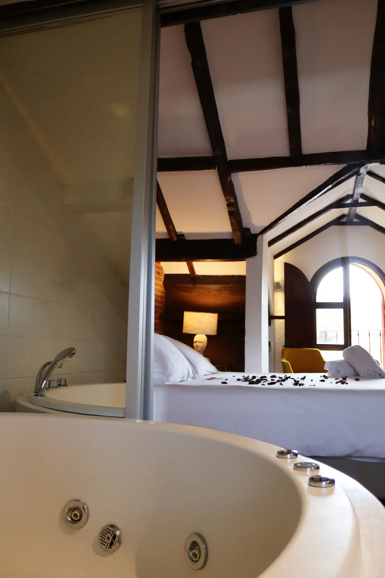 Vista de un jacuzzi blanco en primer plano dentro de una habitación abuhardillada, con una cama doble al fondo