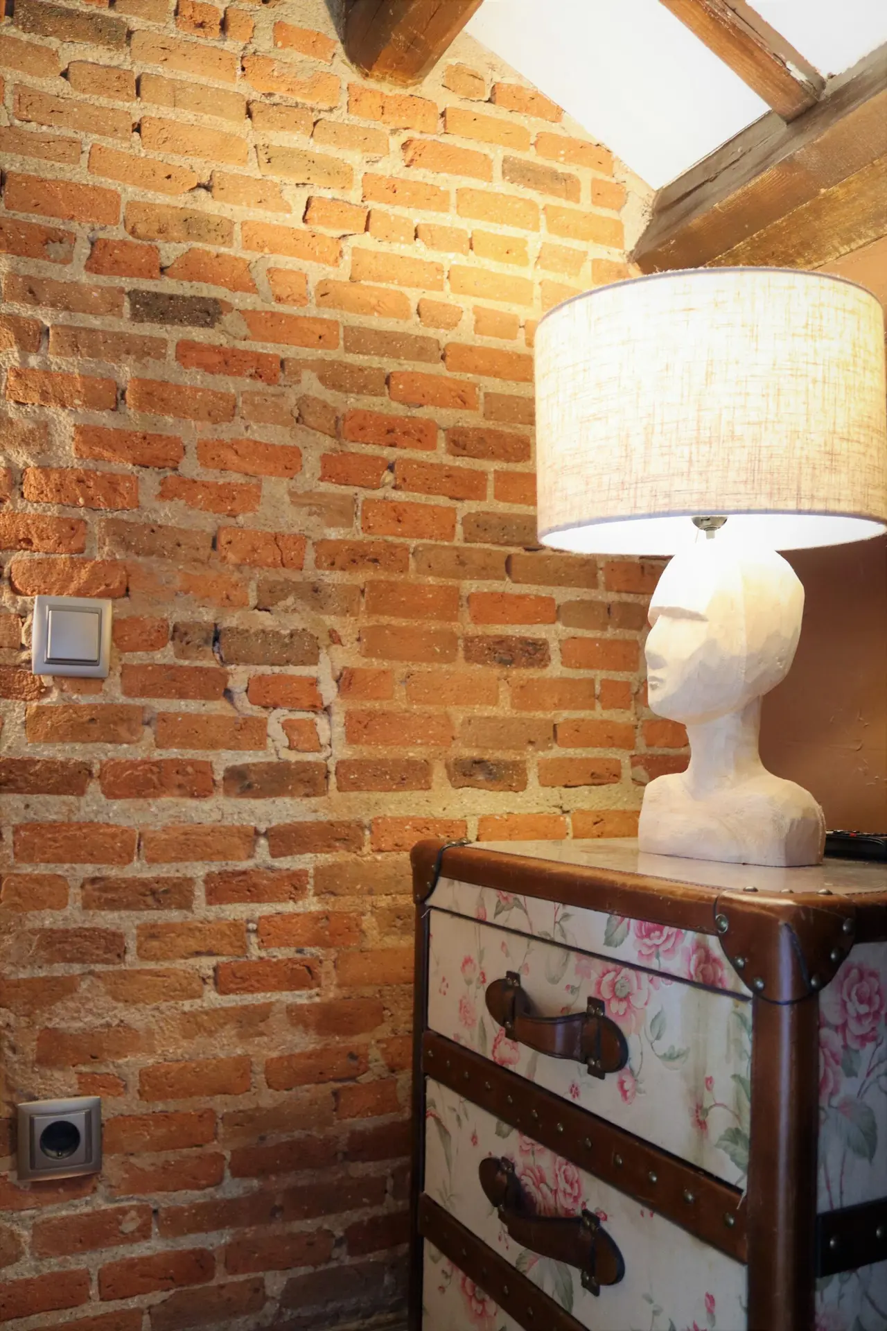 Interior de habitación con pared de ladrillo visto, mueble tipo baúl con cajones decorados con estampado floral