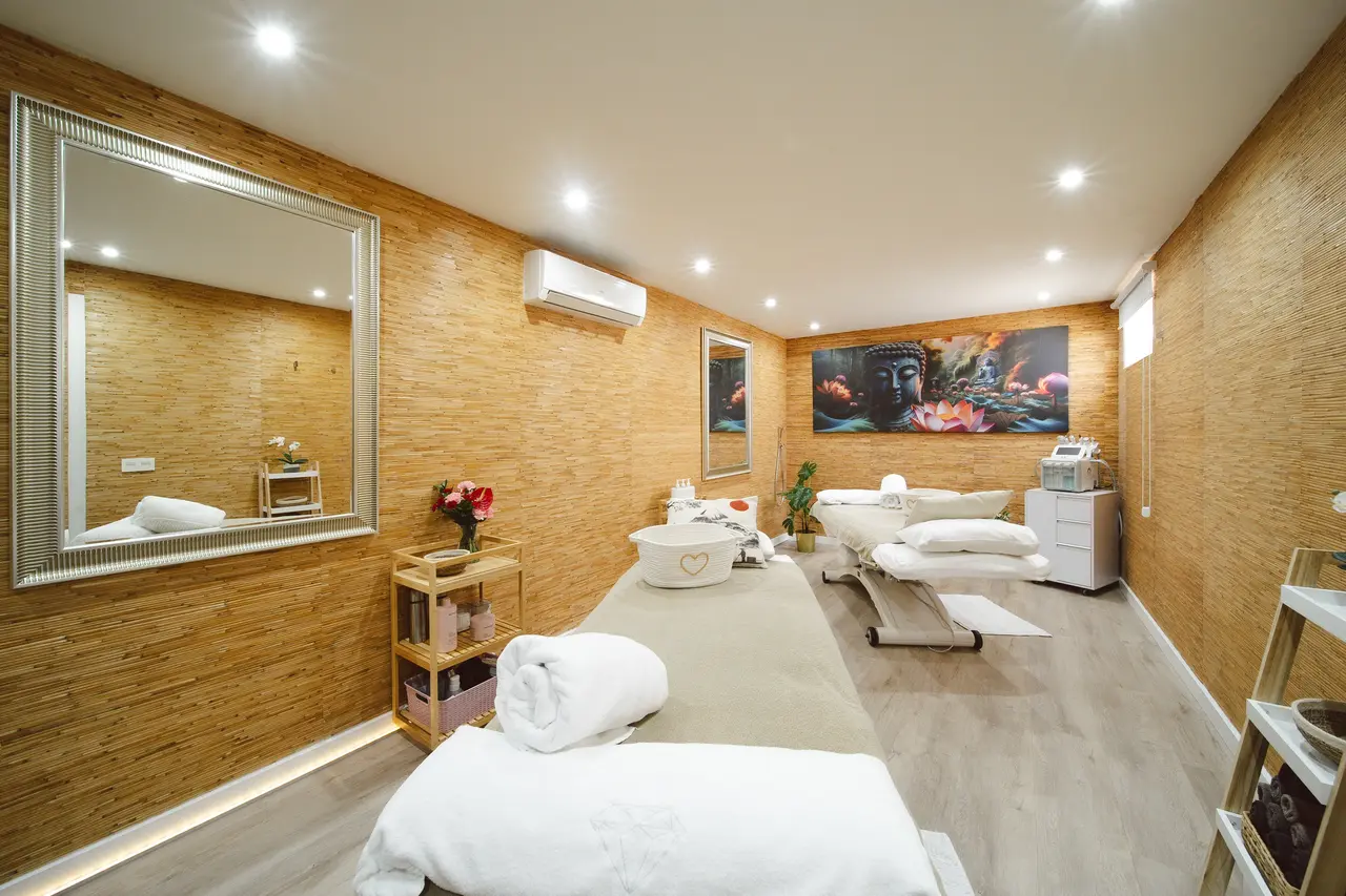 Interior de una sala de masajes o spa con paredes de bambú, dos camillas cubiertas con toallas blancas, un lavabo