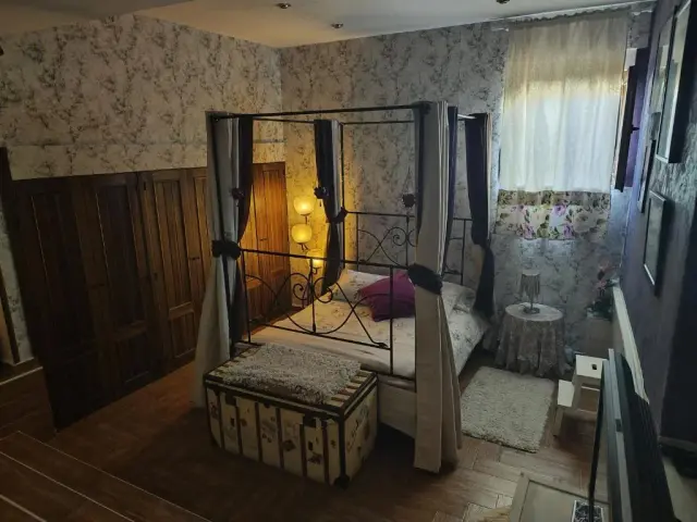 Habitación con cama de dosel de hierro forjado, dosel con cortinas, papel pintado floral en las paredes, armario