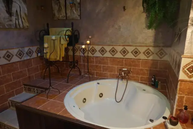 Jacuzzi blanco empotrado en un baño con paredes de azulejos terracota y una franja decorativa.