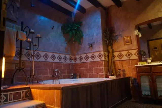 Jacuzzi rectangular empotrado en un baño con paredes de piedra y azulejos decorativos, rodeado de madera, con grifos