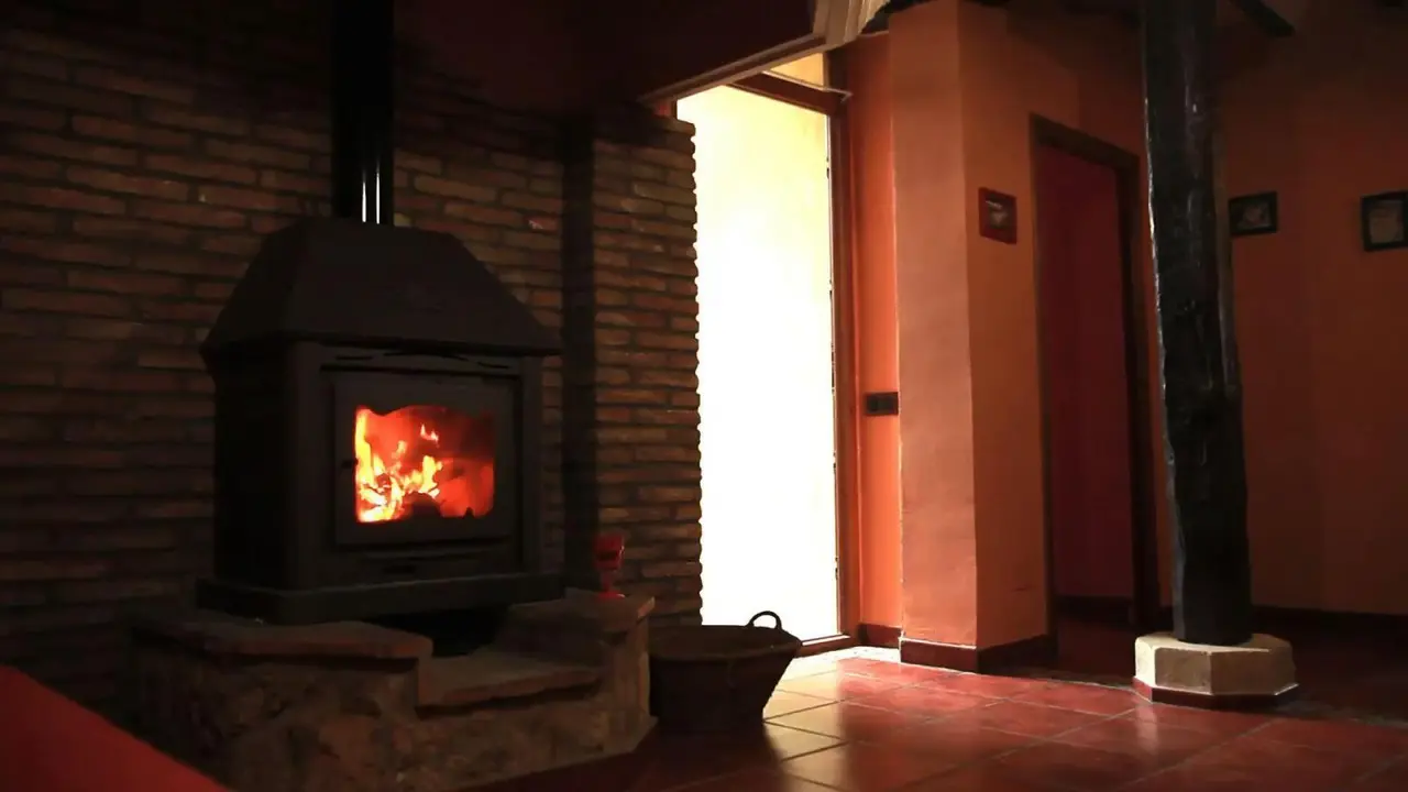 Interior de una habitación con una chimenea de leña encendida en una base de piedra, suelo de terracota, paredes