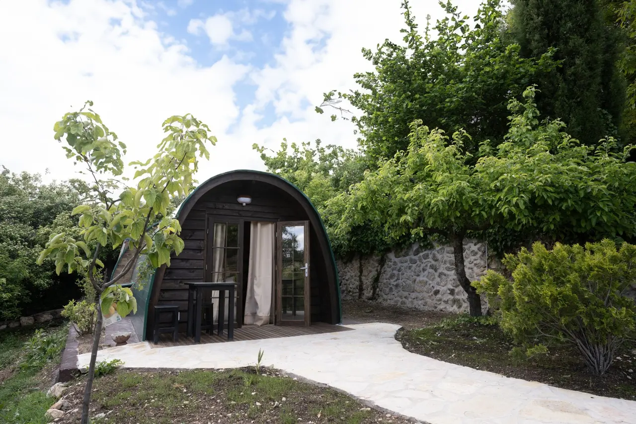 Vista exterior de una cabaña tipo iglú de madera oscura con puerta abierta y cortina, situada en un jardín