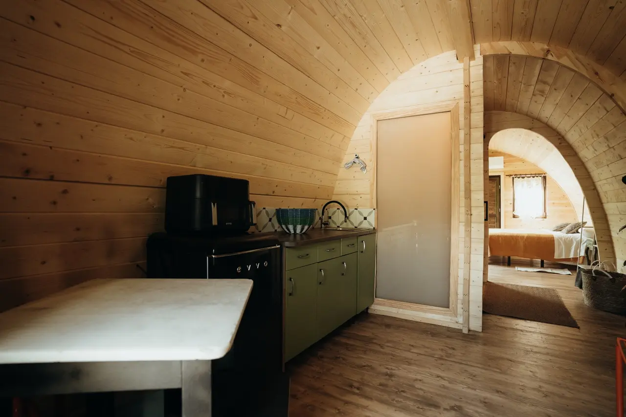Interior de cabaña con paredes y techo abovedado de madera clara, cocina compacta con encimera verde, microondas