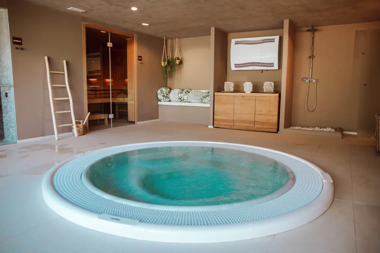 Jacuzzi circular con agua turquesa en un spa privado con sauna, ducha y zona de relax.