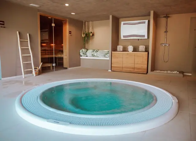 Jacuzzi circular con agua turquesa en un spa privado con ducha, sauna y zona de relax.