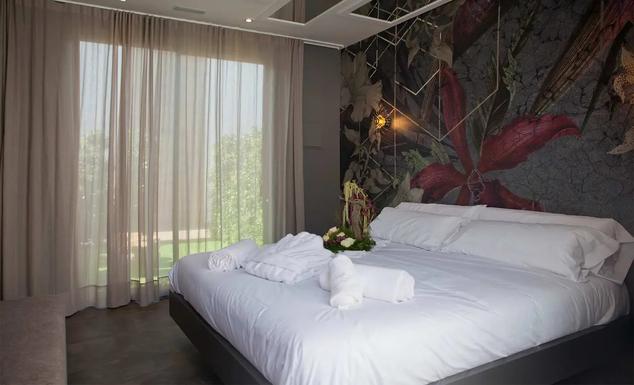 Habitación de hotel con cama grande vestida de blanco, toallas enrolladas y un arreglo floral encima.