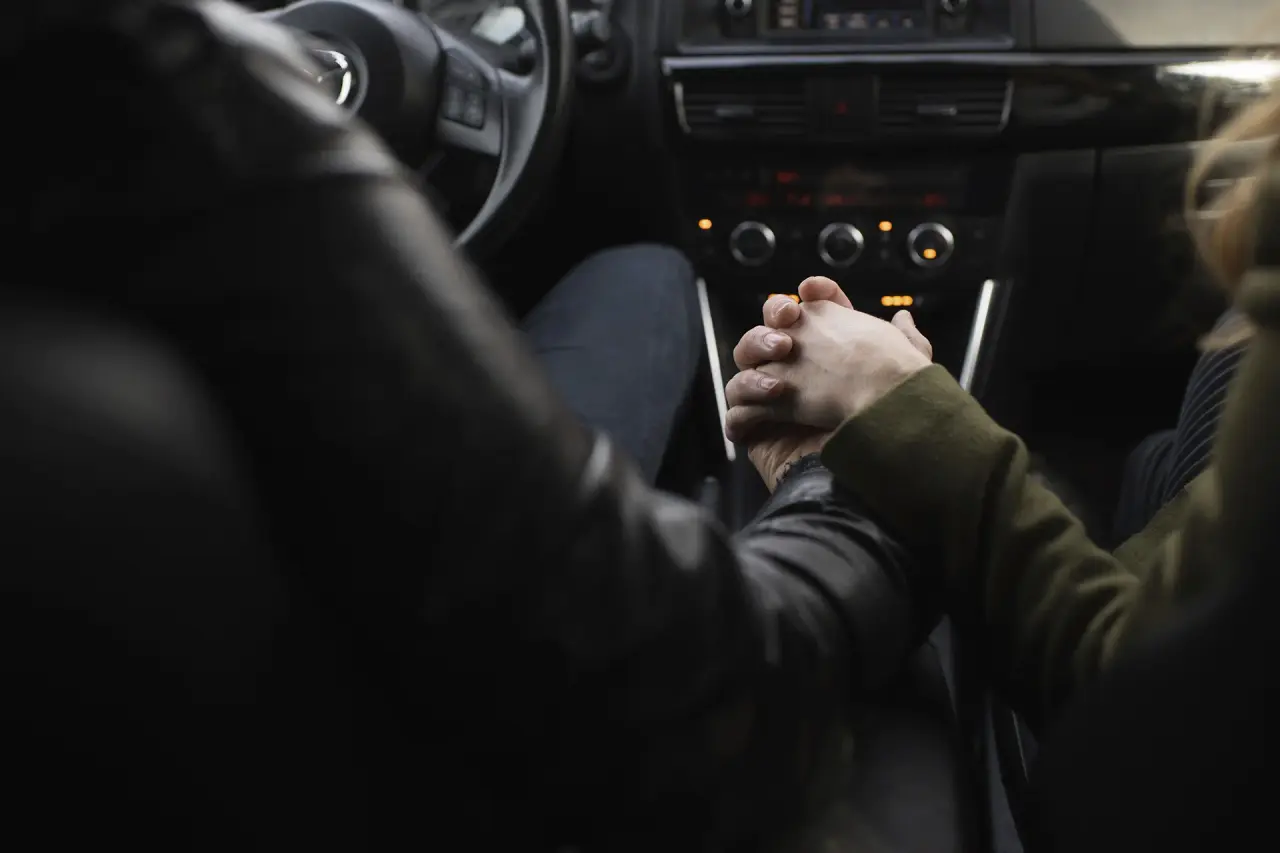 Manos de una pareja entrelazadas en el interior de un coche.