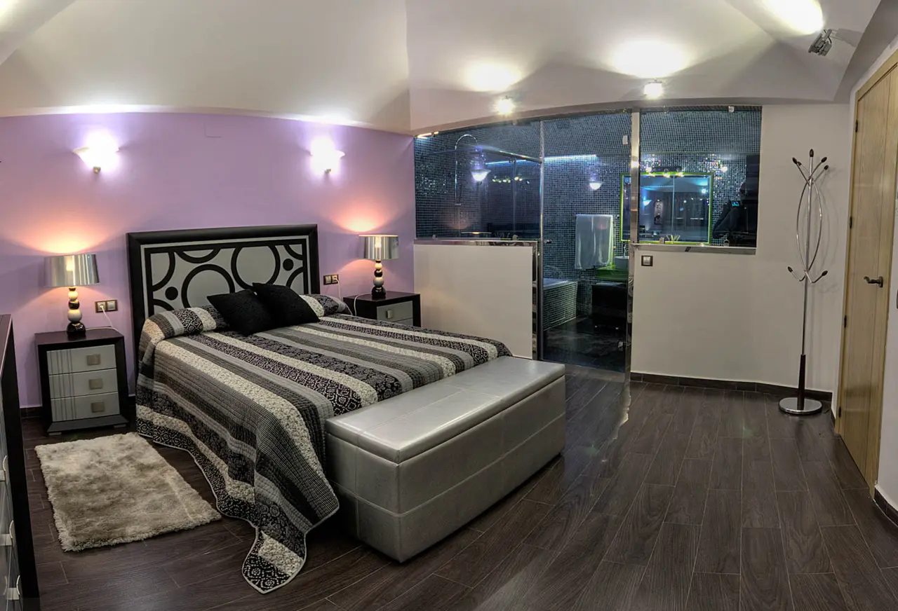Habitación de cabaña con cama doble, cabecero negro decorativo, mesitas de noche con lámparas, banco tapizado al pie