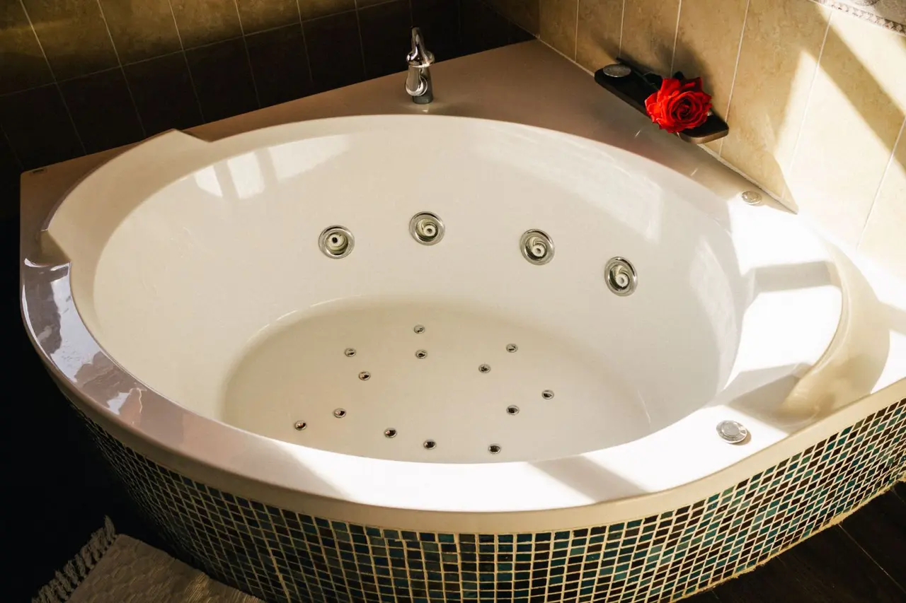 Jacuzzi interior blanco de forma ovalada con múltiples jets en el fondo y laterales, borde decorado con mosaico verde