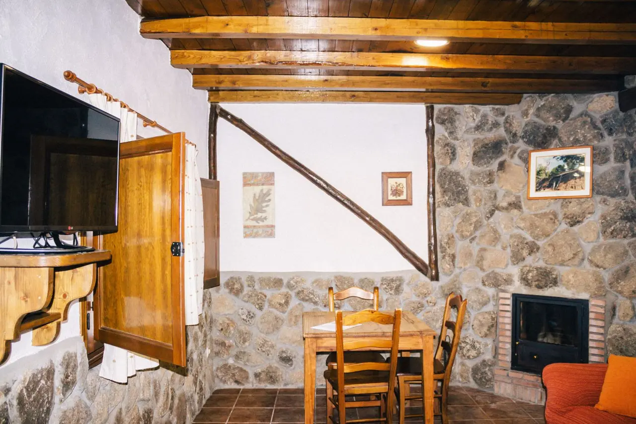 Interior de una habitación rústica con paredes de piedra, techo de madera con vigas vistas, mesa de comedor de madera