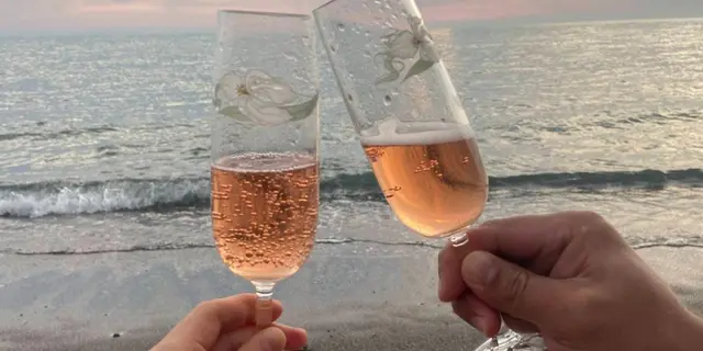 Dos copas de cava rosado brindando frente al mar al atardecer.