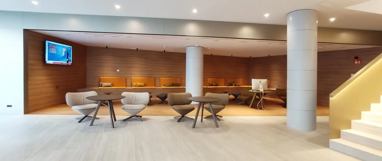 Amplio salón de la suite con zona de estar, mesas y sillones frente a una pared de madera con nichos iluminados