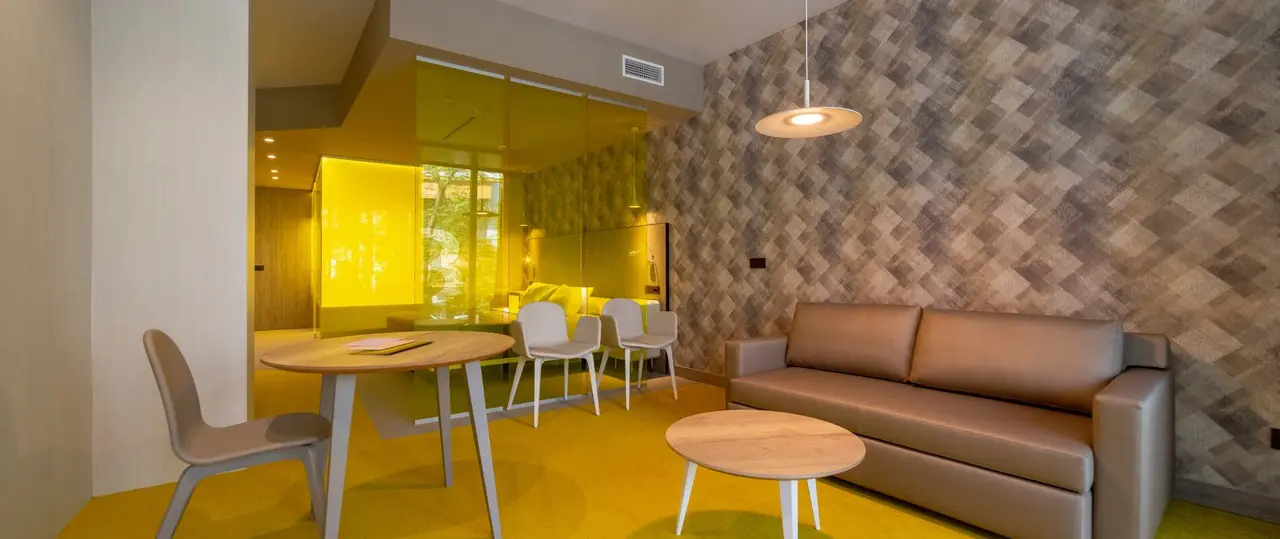 Interior de suite con sofá de cuero, mesa redonda con sillas, mesa de centro y pared con papel geométrico en tonos
