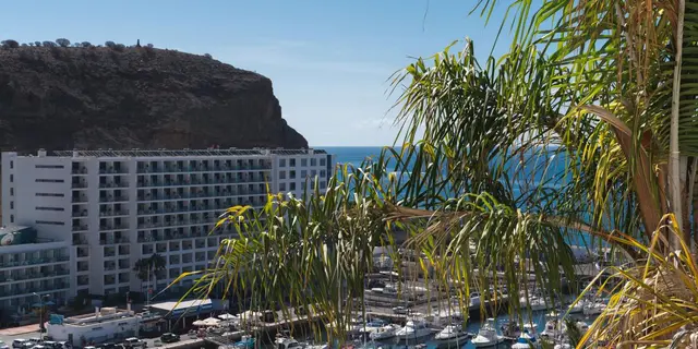Vista panorámica de un puerto deportivo con numerosos barcos amarrados, un edificio blanco de apartamentos