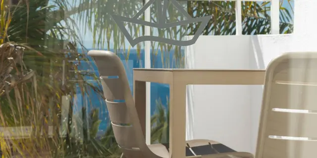 Vista exterior desde una terraza con sillas y mesa de plástico beige, rodeada de vegetación tropical y palmeras