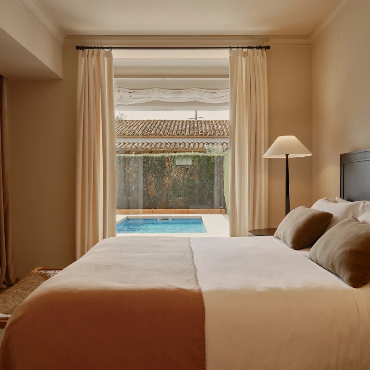 Vista desde el interior de una habitación con cama grande hacia una piscina privada al aire libre, enmarcada