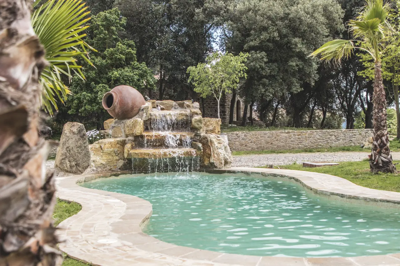 Piscina exterior con cascada de piedra y vegetación alrededor.