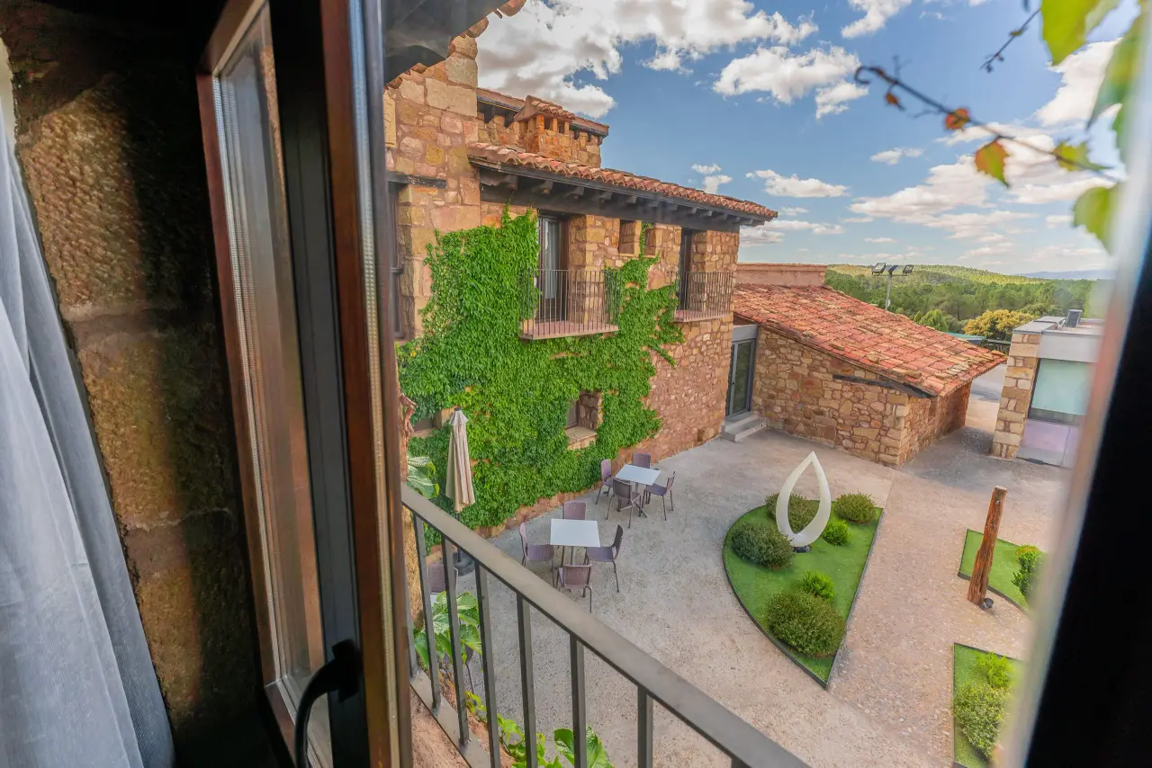 Vista desde una ventana o balcón de una masía de piedra con enredaderas, patio interior con mesas, sillas