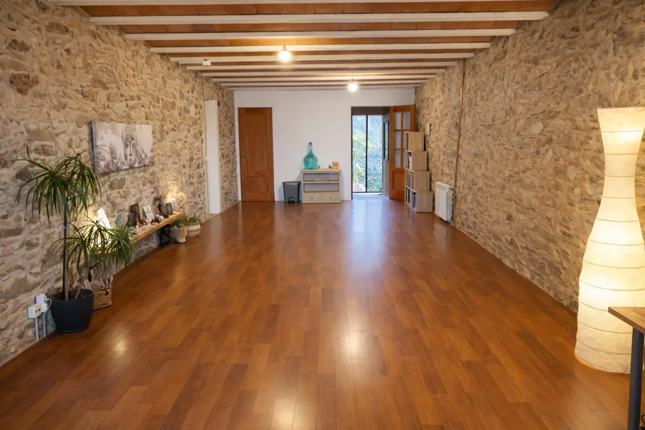 Interior de una amplia habitación con paredes de piedra, techo con vigas de madera, suelo de parquet brillante