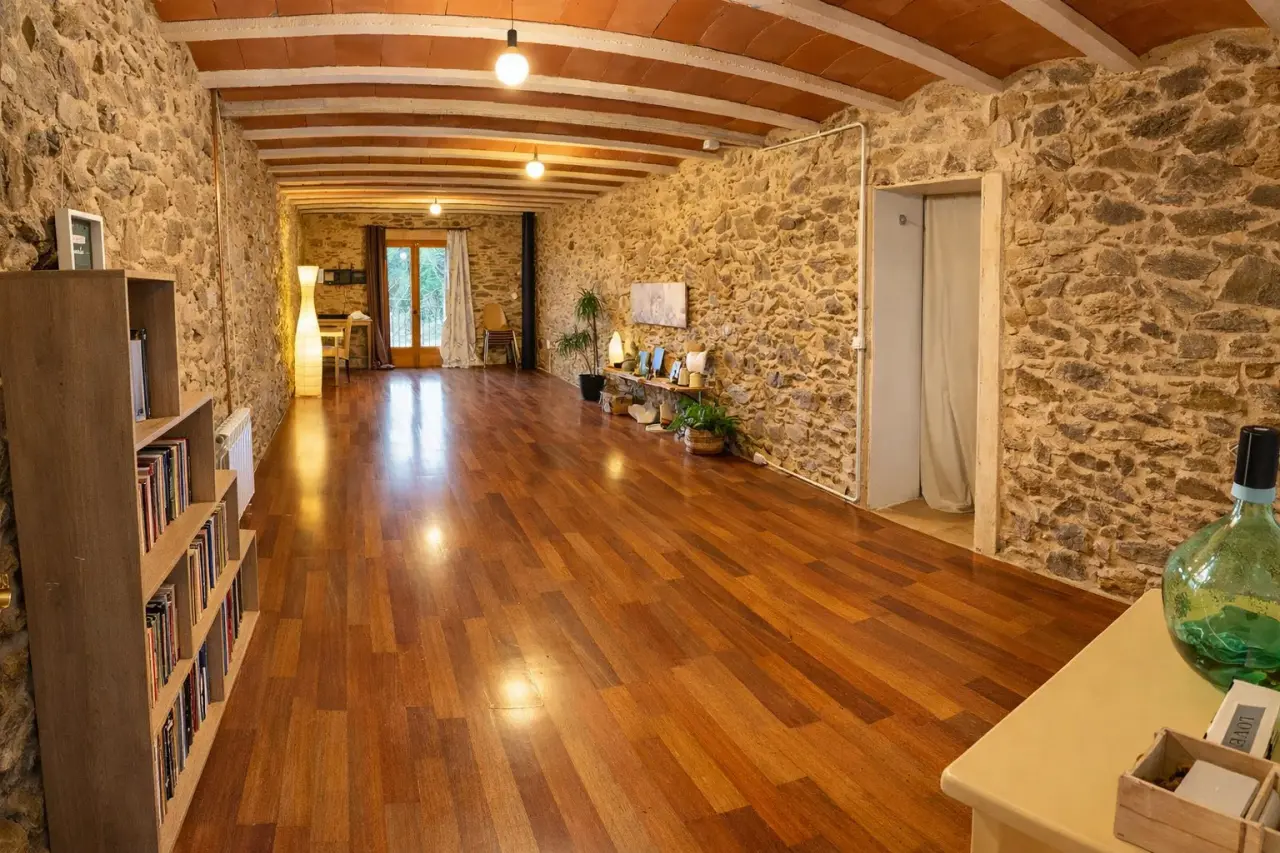 Interior de una sala alargada con paredes de piedra y techo abovedado de madera con vigas vistas.