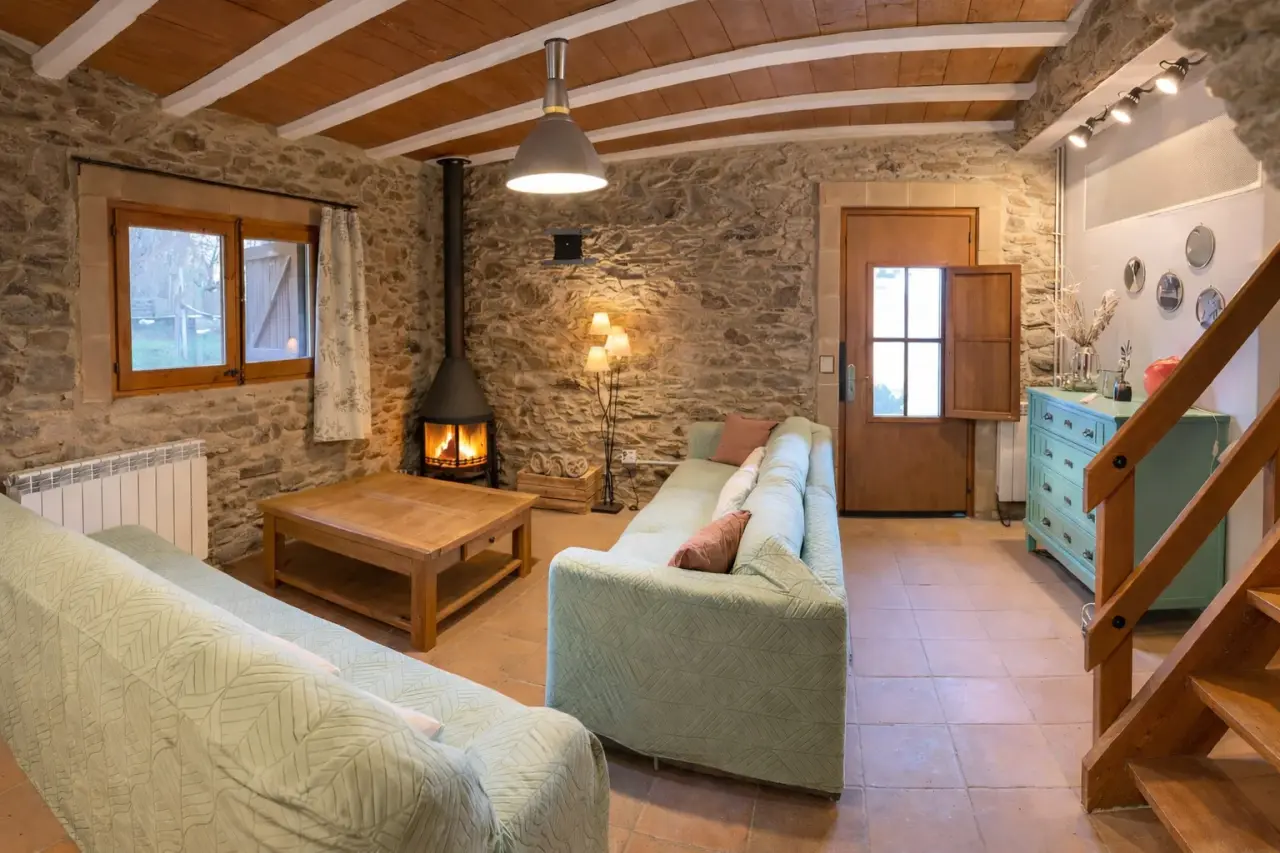 Interior de una sala de estar rústica con paredes de piedra, techo de madera con vigas vistas, dos sofás verdes
