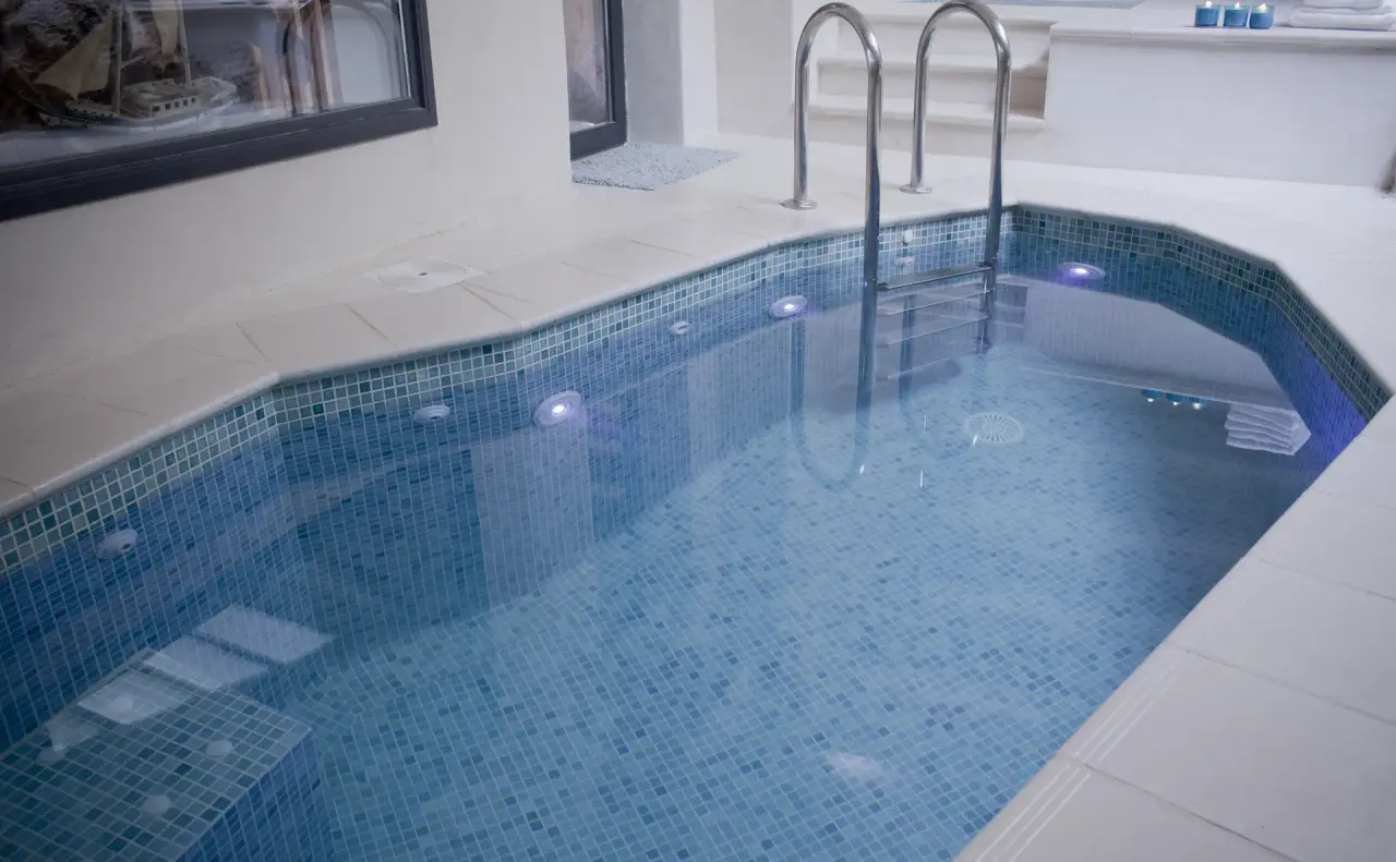 Piscina interior con mosaicos azules, escaleras metálicas y luces subacuáticas en un spa privado.