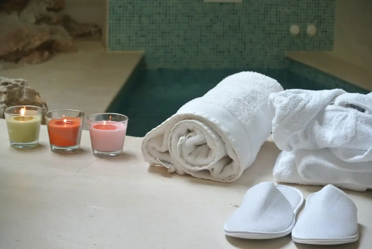 Tres velas encendidas, toallas enrolladas, albornoces y zapatillas dispuestas junto al borde de un spa privado