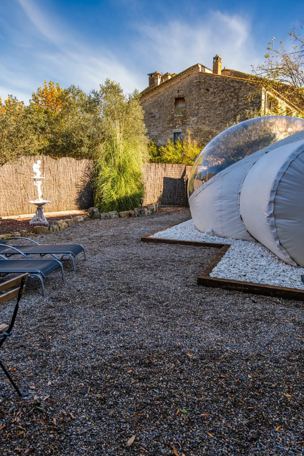 Jacuzzi privado en forma de burbuja inflable transparente ubicado en un patio exterior con grava, rodeado de tumbonas